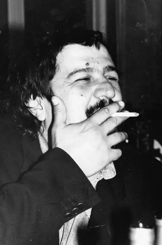 Bogdan Ulmu în tinerețe, fotografie alb-negru: râde cu ochii mijiți, cu o țigară între degete și mâna la bărbie