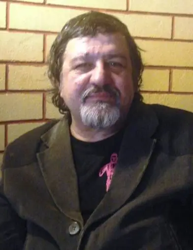 Portret color al lui Bogdan Ulmu: păr cărunt ondulat, mustață și barbă albă, haină închisă la culoare